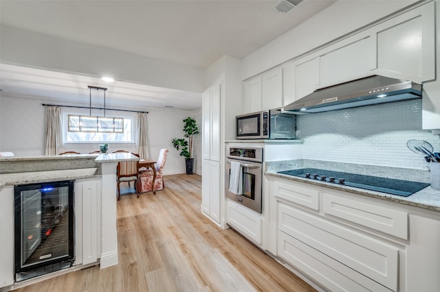 kitchen featuring light wood finished floors, stainless steel appliances, wine cooler, white cabinets, and under cabinet range hood