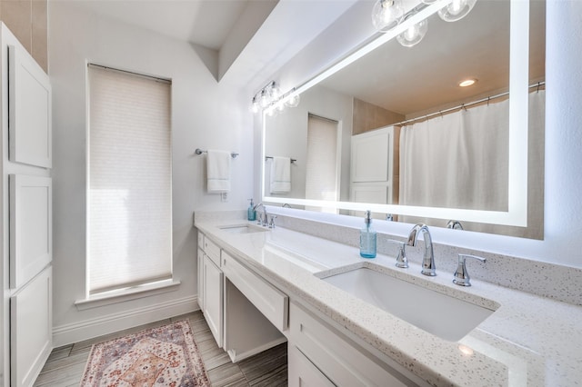 bathroom with double vanity, wood finished floors, baseboards, and a sink