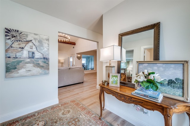 corridor with lofted ceiling, baseboards, light wood finished floors, and a chandelier