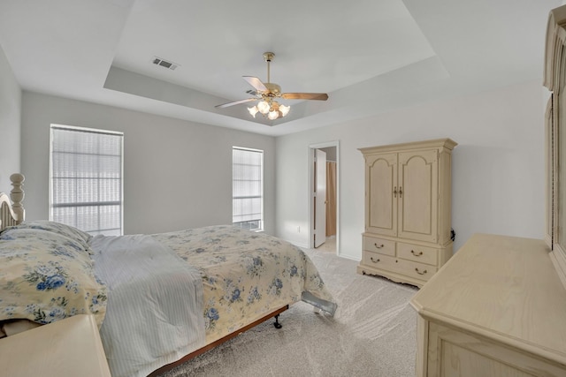 bedroom with visible vents, a raised ceiling, light carpet, and a ceiling fan