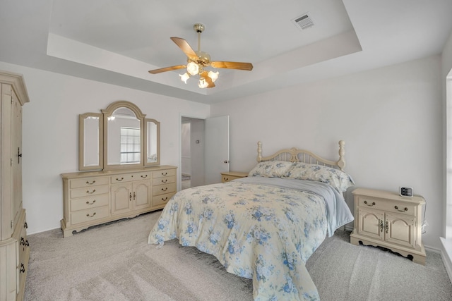 bedroom featuring a tray ceiling, light colored carpet, and visible vents