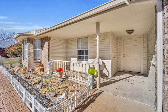 entrance to property with brick siding, a porch, and fence