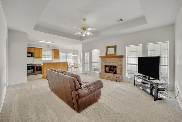 living room featuring a raised ceiling, light colored carpet, visible vents, and ceiling fan