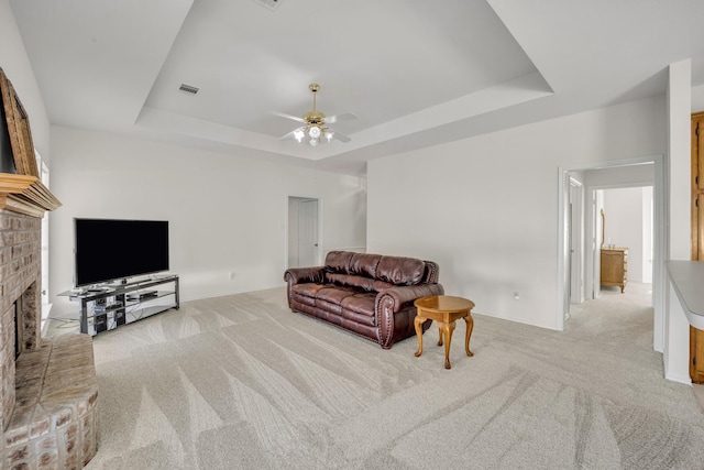 living area featuring a tray ceiling, a brick fireplace, carpet, and visible vents