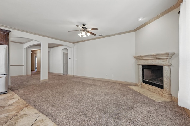 unfurnished living room featuring arched walkways, a fireplace, baseboards, light colored carpet, and ceiling fan