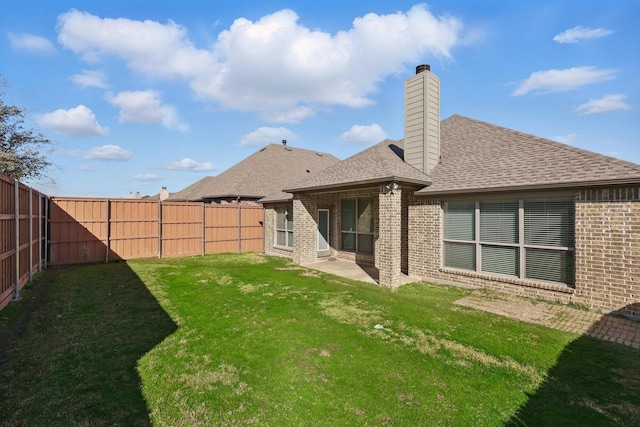 rear view of house featuring a yard, a fenced backyard, a shingled roof, a chimney, and brick siding