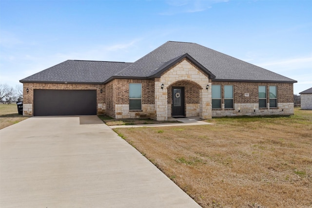 french country inspired facade featuring a front yard, an attached garage, a shingled roof, concrete driveway, and brick siding