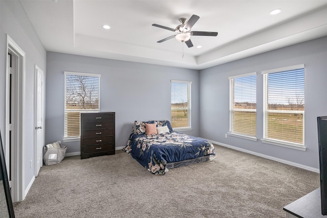 carpeted bedroom with a raised ceiling, multiple windows, and baseboards