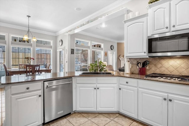 kitchen featuring backsplash, dark stone counters, ornamental molding, appliances with stainless steel finishes, and a sink