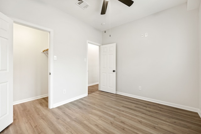 unfurnished bedroom featuring light wood finished floors, visible vents, a walk in closet, baseboards, and a closet