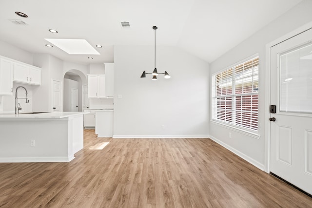 unfurnished living room with visible vents, lofted ceiling with skylight, light wood-type flooring, a sink, and baseboards