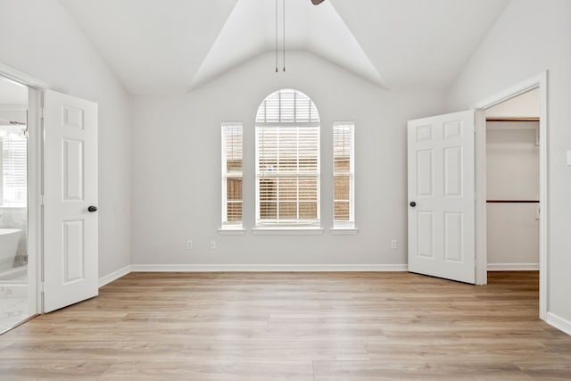 unfurnished bedroom with a walk in closet, vaulted ceiling, light wood-style floors, and ensuite bathroom