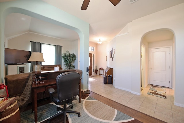office area with arched walkways, a ceiling fan, tile patterned floors, and baseboards