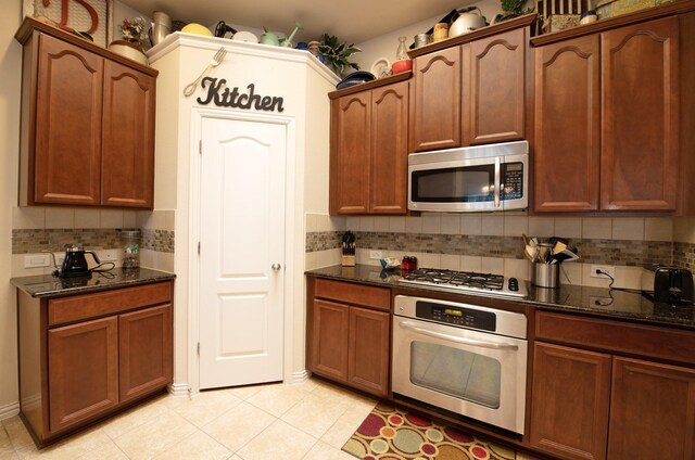 kitchen with dark stone counters, light tile patterned flooring, appliances with stainless steel finishes, and tasteful backsplash