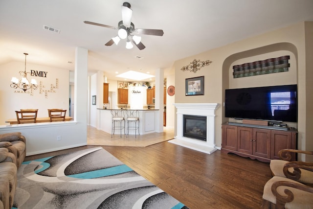 living room with a glass covered fireplace, visible vents, baseboards, ceiling fan with notable chandelier, and wood finished floors