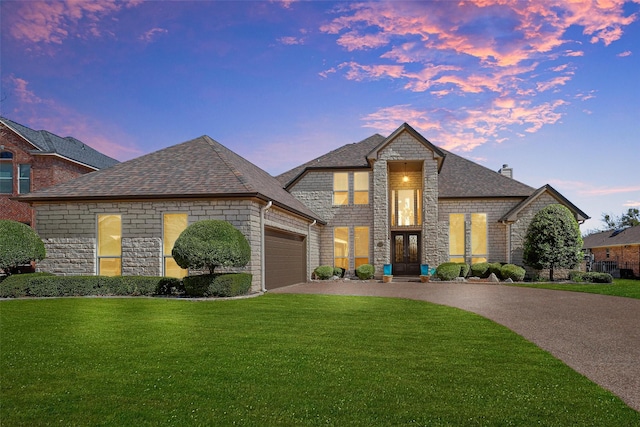 french country home with driveway, an attached garage, a front yard, and a shingled roof