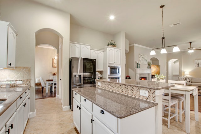 kitchen featuring a kitchen island, open floor plan, stainless steel appliances, arched walkways, and decorative backsplash