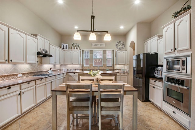 kitchen featuring under cabinet range hood, stainless steel appliances, arched walkways, decorative backsplash, and hanging light fixtures