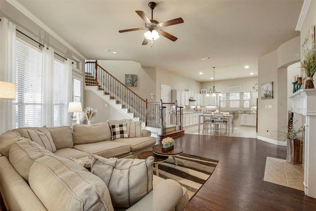 living area featuring visible vents, a ceiling fan, wood finished floors, baseboards, and stairs