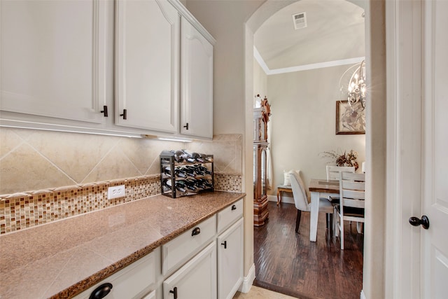 kitchen with light wood finished floors, visible vents, backsplash, crown molding, and white cabinetry