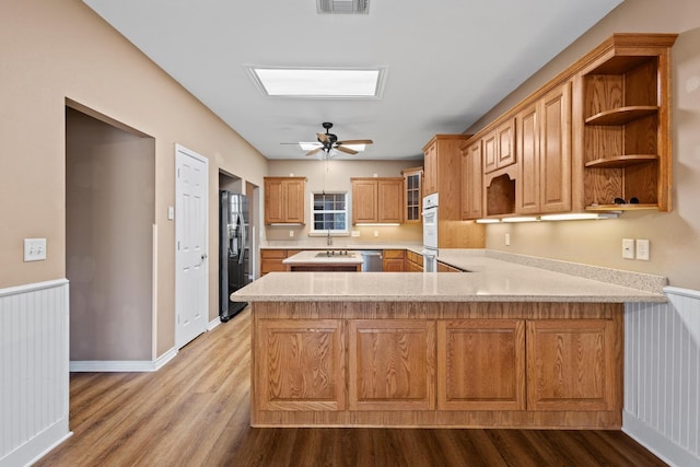 kitchen with a ceiling fan, wood finished floors, a peninsula, glass insert cabinets, and fridge with ice dispenser