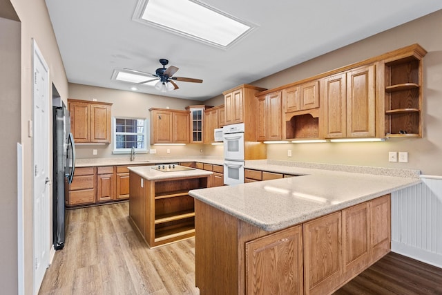 kitchen with open shelves, light wood-type flooring, a peninsula, white appliances, and a sink