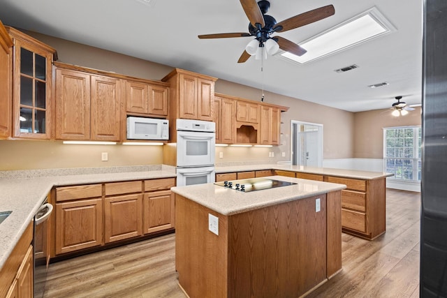 kitchen with white appliances, visible vents, a peninsula, glass insert cabinets, and light wood-style floors