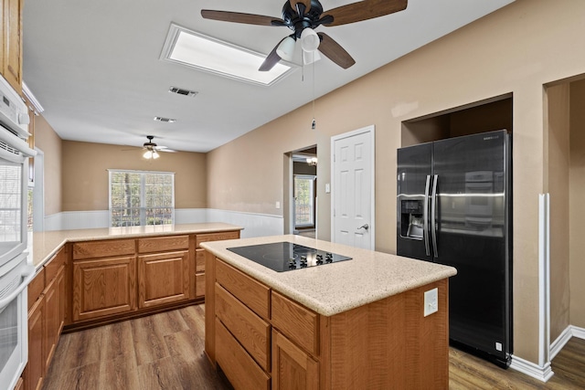 kitchen with a kitchen island, black appliances, visible vents, and wood finished floors