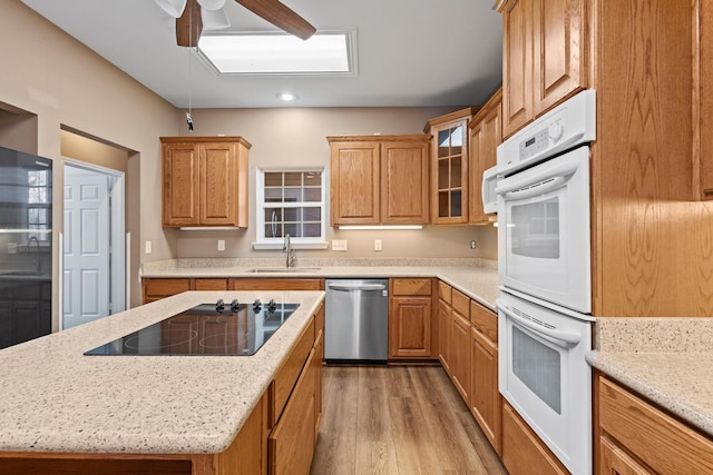 kitchen featuring double oven, dishwasher, light wood-type flooring, black electric cooktop, and a sink