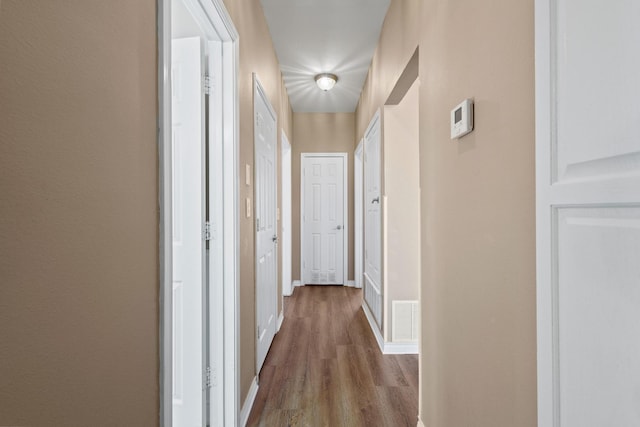 corridor with dark wood-style floors, visible vents, and baseboards