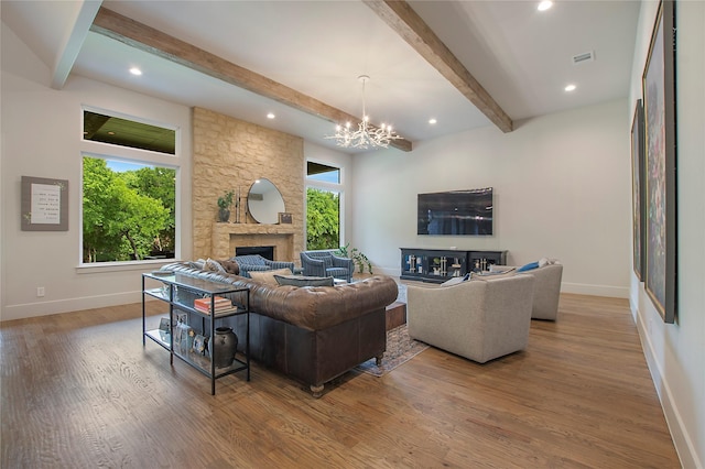 living room featuring a stone fireplace, an inviting chandelier, visible vents, and wood finished floors