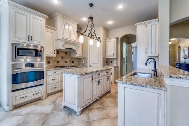 kitchen featuring a sink, arched walkways, appliances with stainless steel finishes, decorative backsplash, and custom exhaust hood