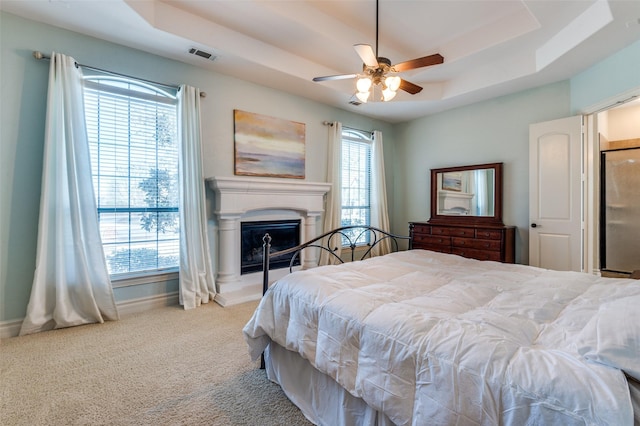 carpeted bedroom with a tray ceiling, baseboards, visible vents, and a fireplace with raised hearth