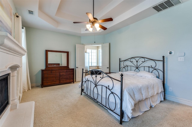 bedroom featuring carpet, a raised ceiling, a fireplace with raised hearth, and visible vents