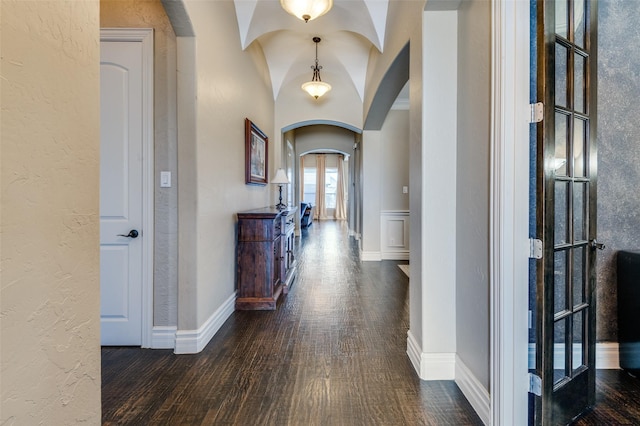 corridor featuring a textured wall, baseboards, arched walkways, and dark wood-style flooring