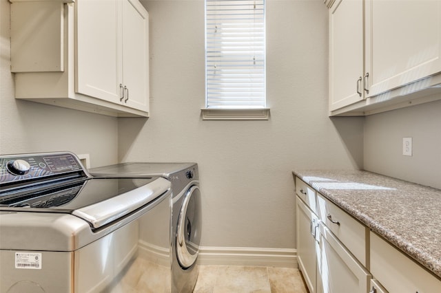 clothes washing area with cabinet space, light tile patterned floors, washing machine and dryer, and baseboards