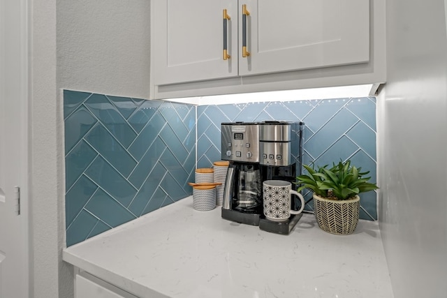 room details featuring decorative backsplash, white cabinetry, and light stone countertops