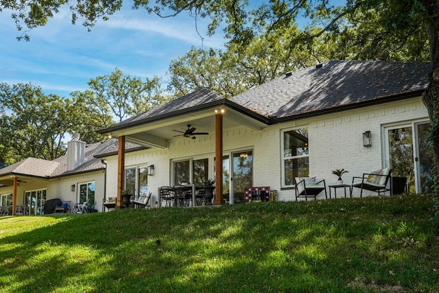 rear view of property featuring a ceiling fan, a yard, a chimney, a patio area, and brick siding