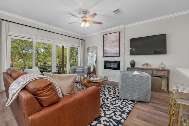 living room with visible vents, crown molding, ceiling fan, a fireplace, and wood finished floors