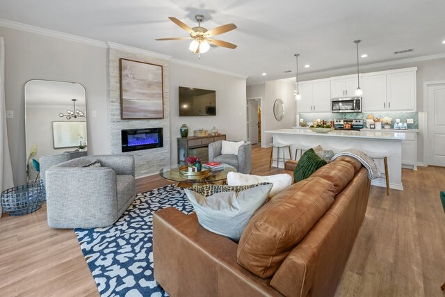 living area featuring visible vents, a large fireplace, light wood-type flooring, and ornamental molding