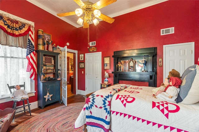 bedroom featuring visible vents, wood finished floors, a high ceiling, and ornamental molding