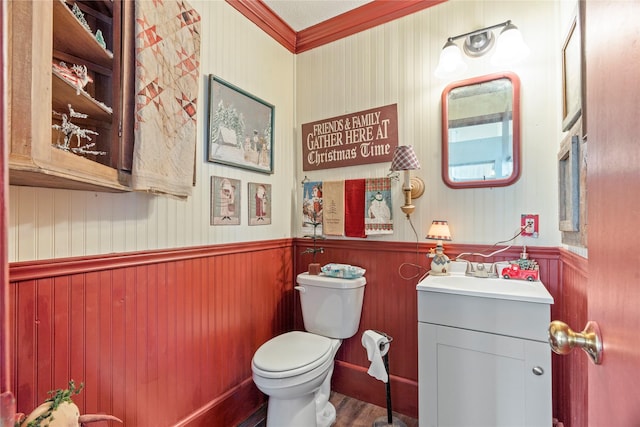 bathroom with toilet, wainscoting, wood finished floors, vanity, and ornamental molding