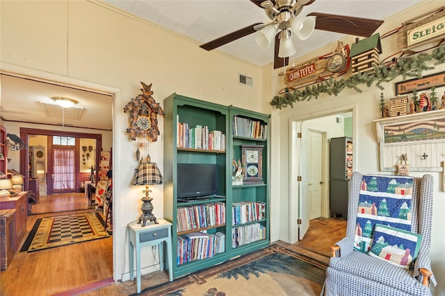 living room featuring attic access, visible vents, a ceiling fan, wood finished floors, and ornamental molding