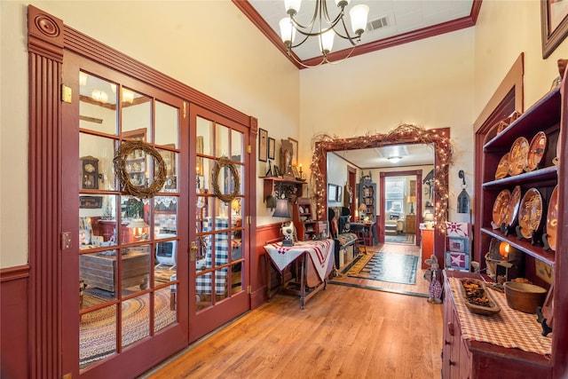interior space featuring an inviting chandelier, wood finished floors, visible vents, ornamental molding, and french doors