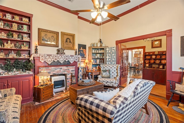 living area with wood-type flooring, crown molding, a ceiling fan, and a fireplace