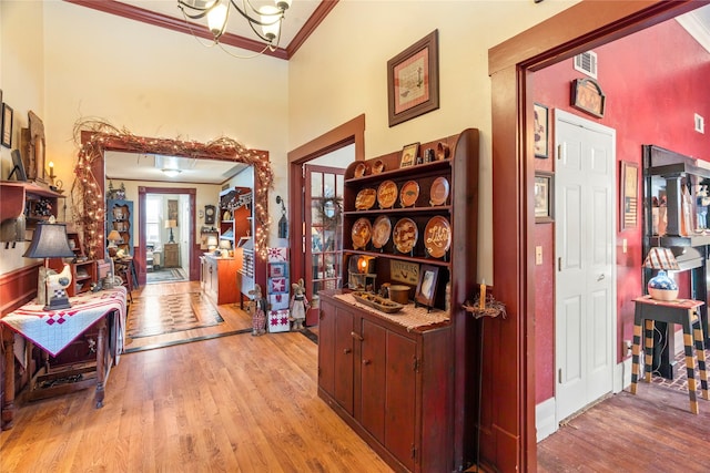corridor featuring crown molding, light wood finished floors, a high ceiling, a notable chandelier, and visible vents