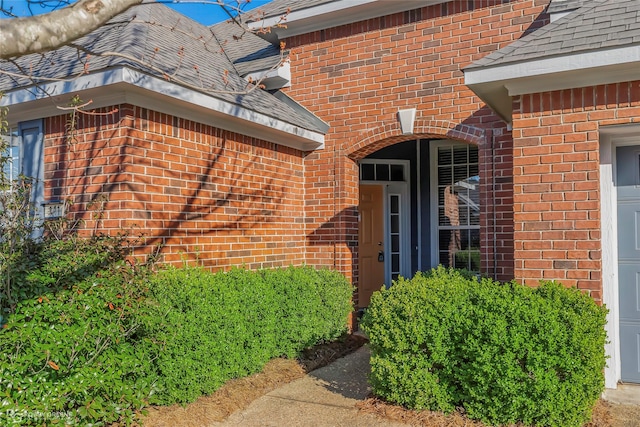 doorway to property featuring a garage, brick siding, and a shingled roof