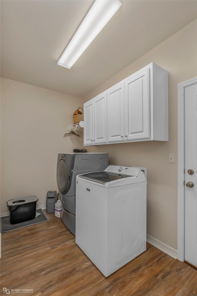 washroom featuring cabinet space, separate washer and dryer, light wood-type flooring, and baseboards