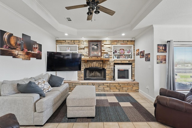 living area featuring visible vents, ornamental molding, a stone fireplace, a raised ceiling, and tile patterned floors