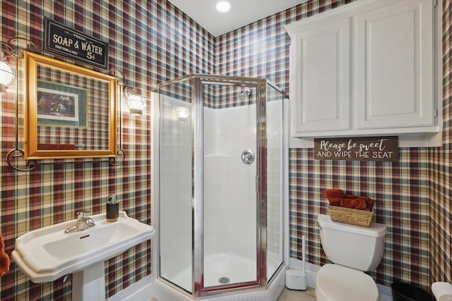 bathroom featuring wallpapered walls, a stall shower, and a sink